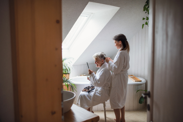 A happy senior mother in bathrobe with adult daughter indoors at home, selfcare concept.