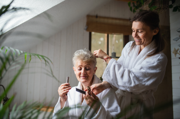 A happy senior mother in bathrobe with adult daughter indoors at home, selfcare concept.