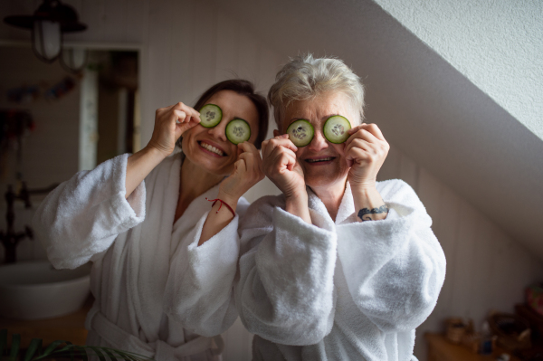 A happy senior mother in bathrobe with adult daughter indoors at home, selfcare concept.