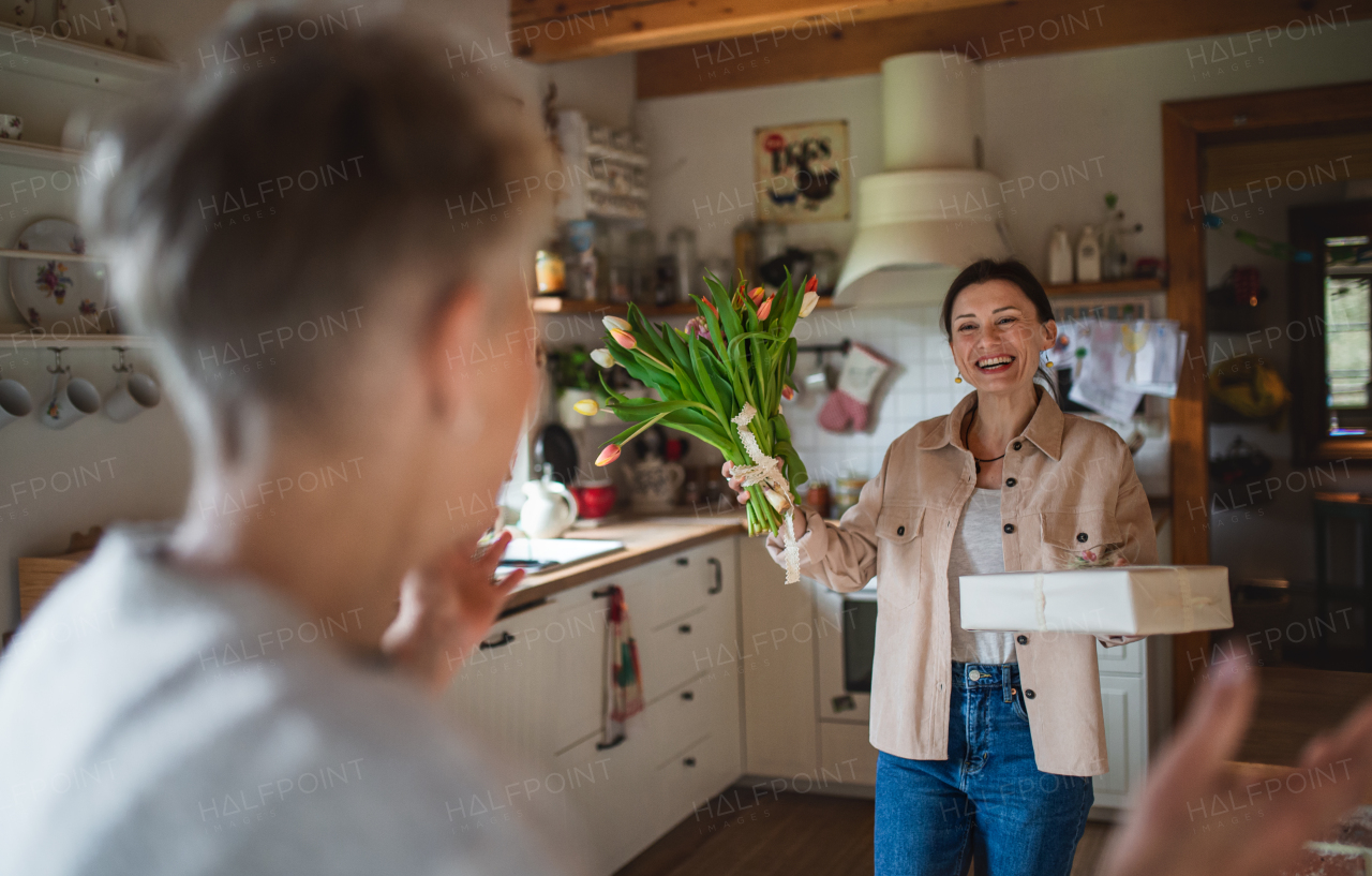 An adult daughter visiting happy senior mother indoors at home, mothers day or birthday celebration.