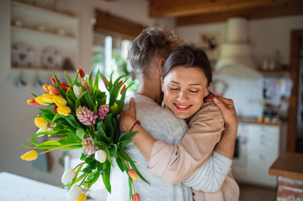 A happy senior mother hugging adult daughter indoors at home, mothers day or birthday celebration.