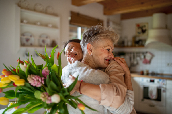 A happy senior mother hugging adult daughter indoors at home, mothers day or birthday celebration.