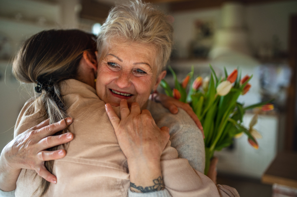 A happy senior mother hugging adult daughter indoors at home, mothers day or birthday celebration.