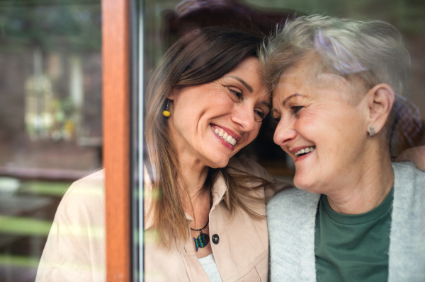 A close-up portrait of happy senior mother with adult daughter indoors at home, hugging and laughing.