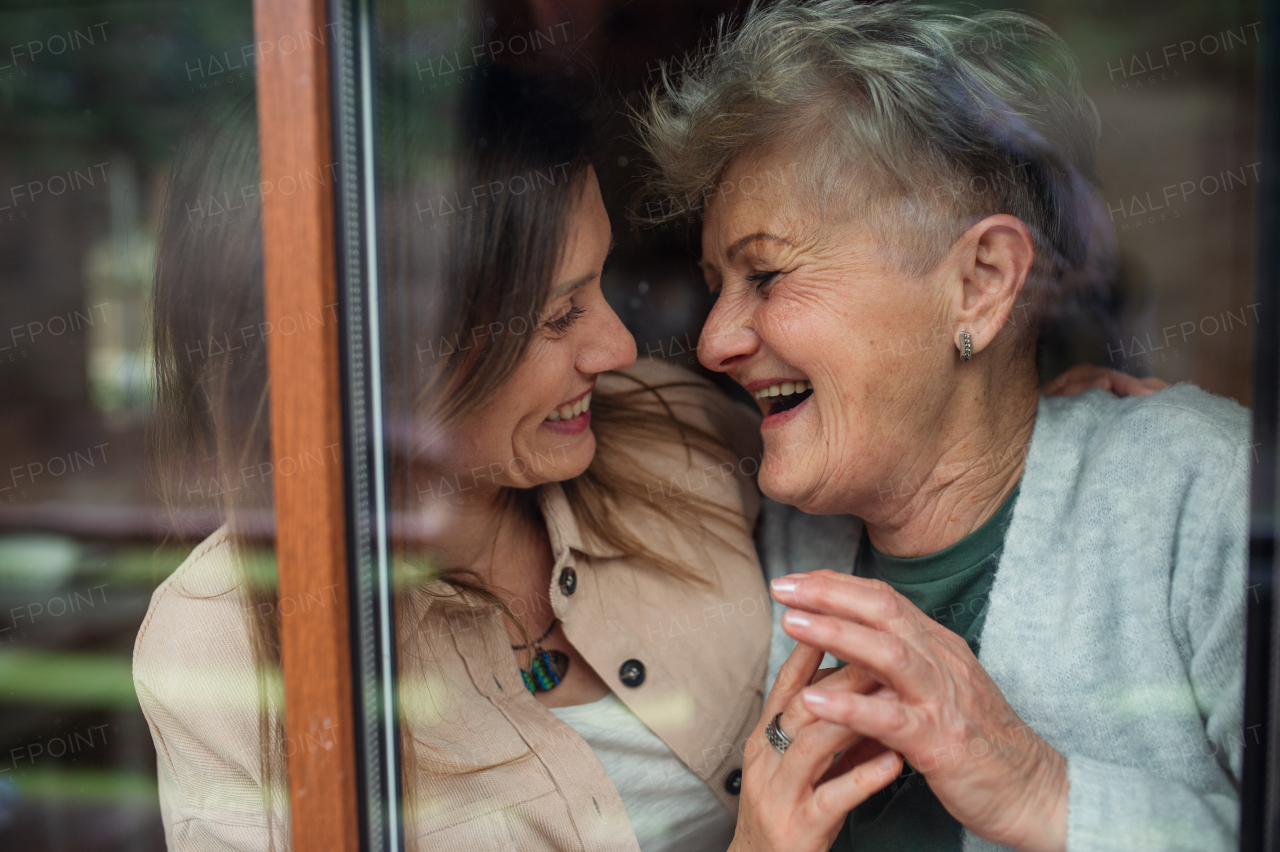 A close-up portrait of happy senior mother with adult daughter indoors at home, hugging and laughing.