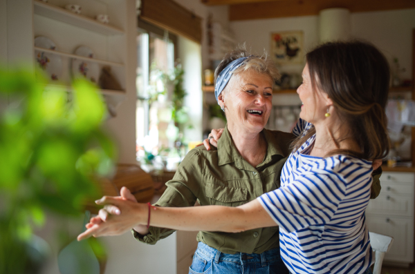 A happy senior mother having fun with adult daughter indoors at home, dancing.