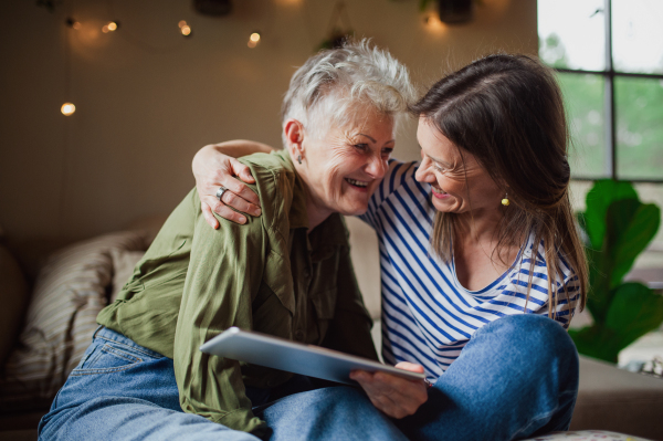 A portrait of happy senior mother with adult daughter indoors at home, using tablet.