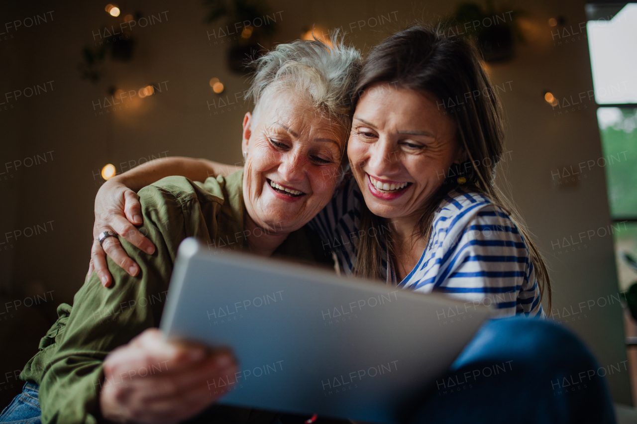 A portrait of happy senior mother with adult daughter indoors at home, using tablet.