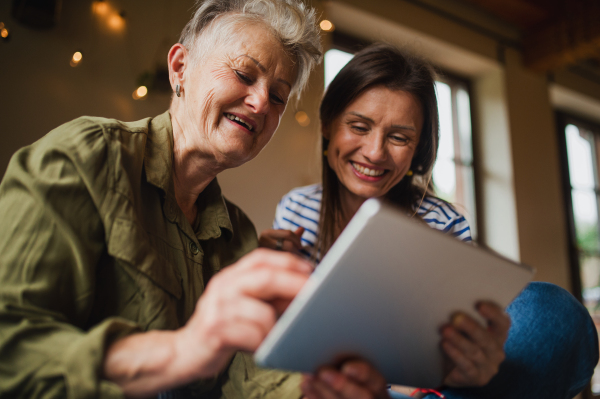 A portrait of happy senior mother with adult daughter indoors at home, using tablet.