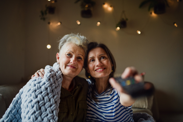 A portrait of happy senior mother with adult daughter indoors at home, watching TV.