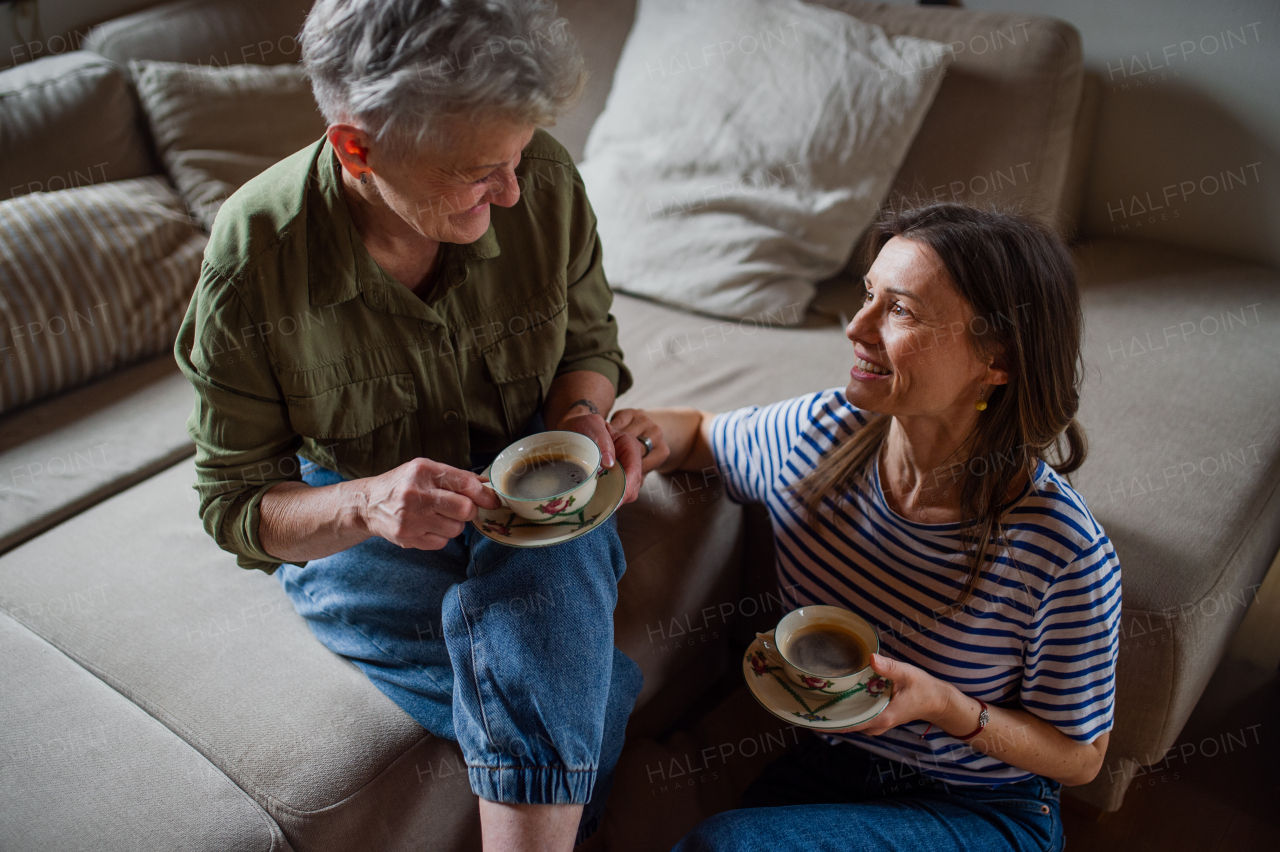 A happy senior mother drinking coffee with adult daughter indoors at home, talking.