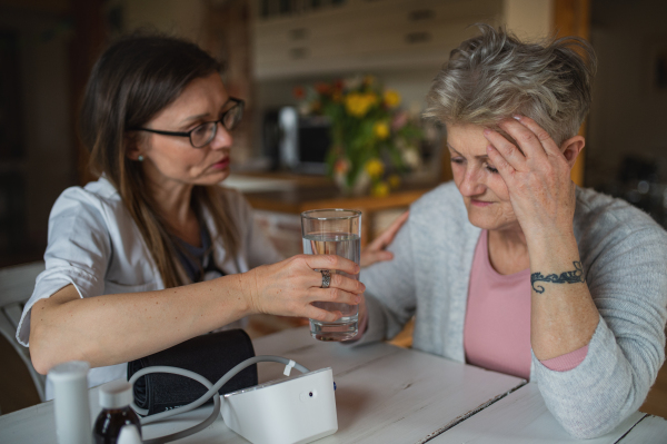 A healthcare worker or caregiver visiting senior woman indoors at home, explaining.