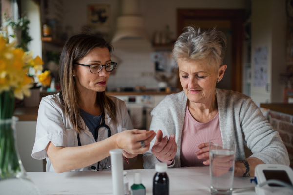 A healthcare worker or caregiver visiting senior woman indoors at home, explaining.