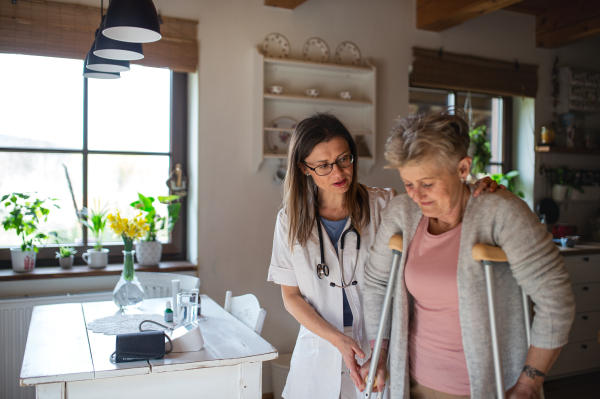 A healthcare worker or caregiver visiting senior woman indoors at home, helping her to walk.