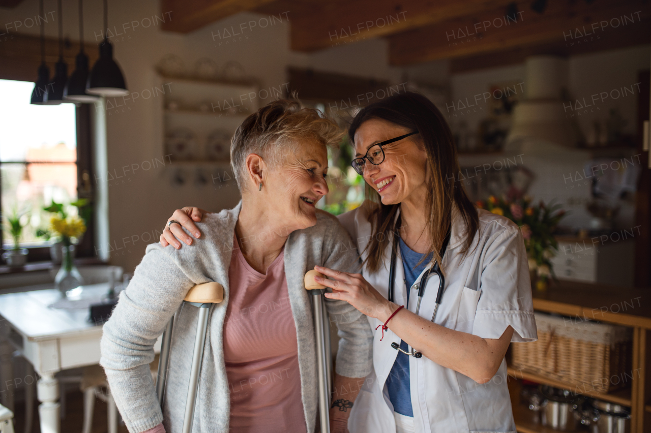 Front view of healthcare worker or a caregiver visiting senior woman indoors at home, helping her to walk.