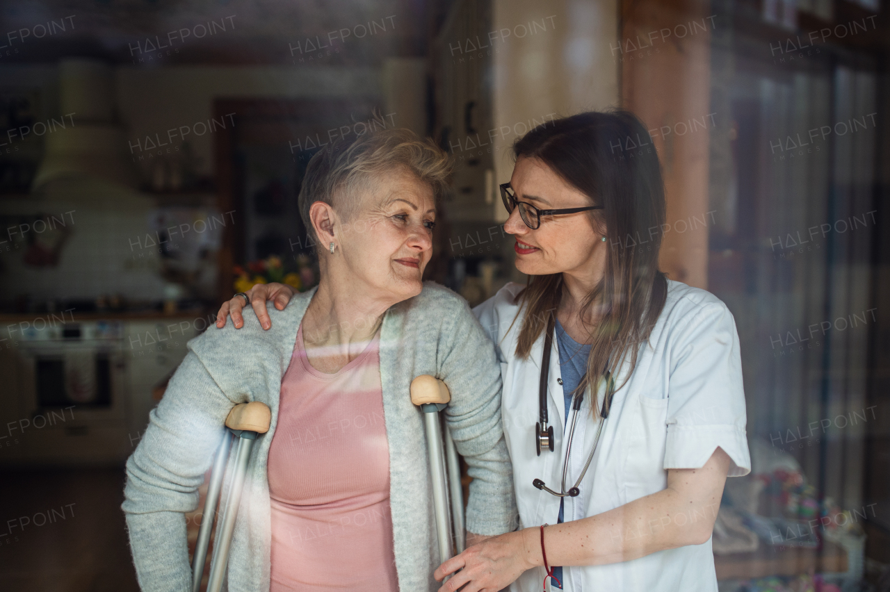 A healthcare worker or caregiver visiting senior woman indoors at home, helping her to walk.