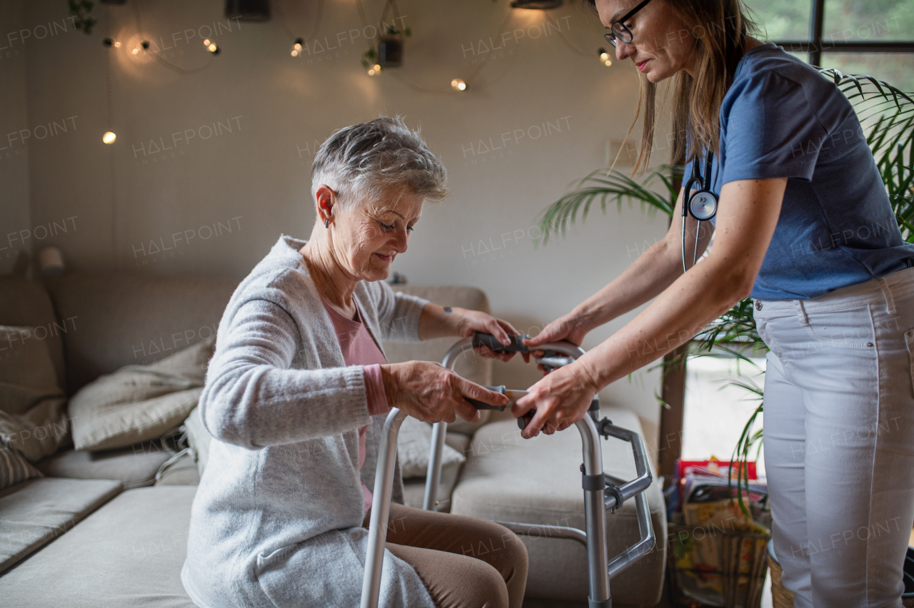 A healthcare worker or caregiver visiting senior woman indoors at home, helping her to walk.