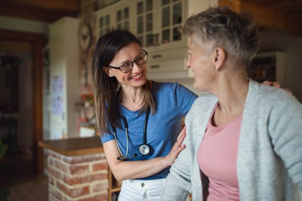 A healthcare worker or caregiver visiting senior woman indoors at home, supporting.