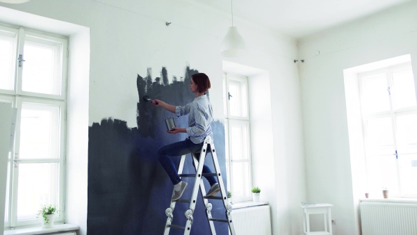 A young woman sitting on ladder painting wall black. A startup of small business.