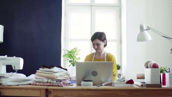 Young creative woman with laptop working in a studio, startup of small tailoring business.