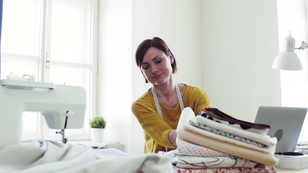 Young creative woman with laptop working in a studio, startup of small tailoring business.