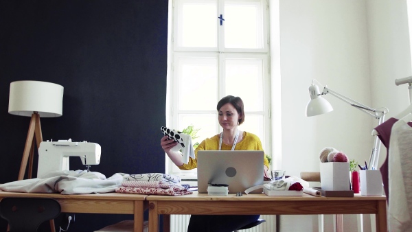 Young creative woman with laptop working in a studio, startup of small tailoring business.