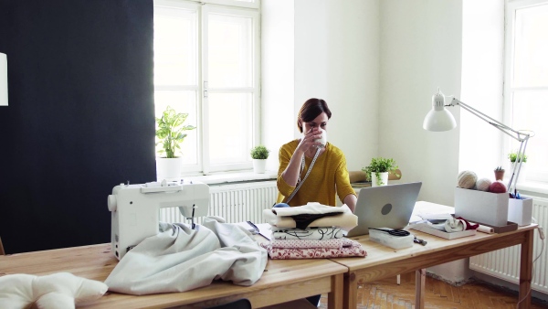 Young creative woman with laptop working in a studio, startup of small tailoring business.