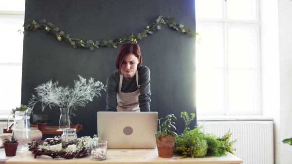 A young creative woman arranging flowers in a flower shop, using laptop. A startup of florist business.