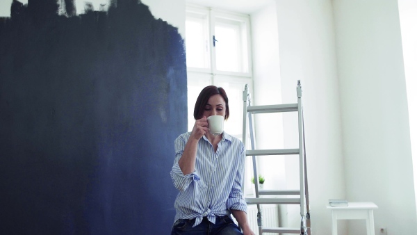 A portrait of young creative woman with a cup of coffee painting wall black. A startup of small business.