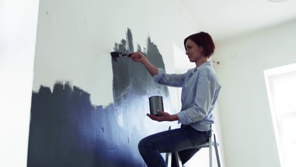 A young woman sitting on ladder painting wall black. A startup of small business.