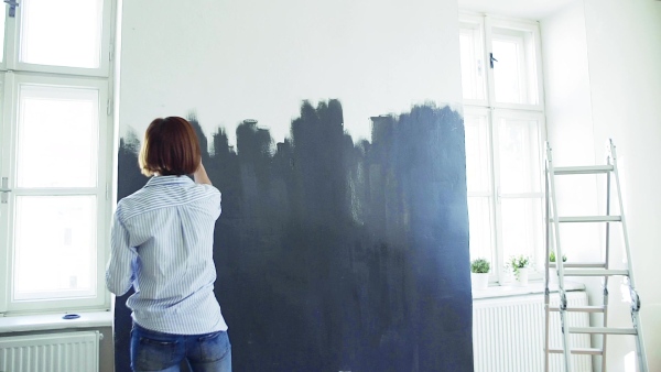 A rear view of young woman painting wall black. A startup of small business. Slow motion.