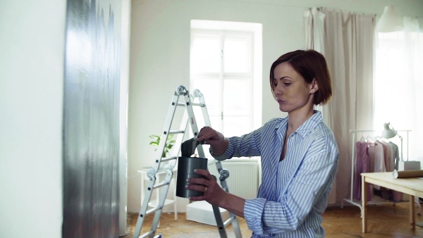 A young woman sitting on ladder painting wall black. A startup of small business. Slow motion.