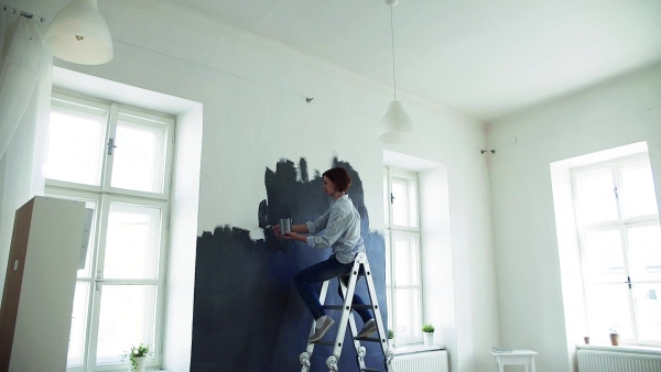 A young woman painting wall black. A startup of small business. Slow motion.