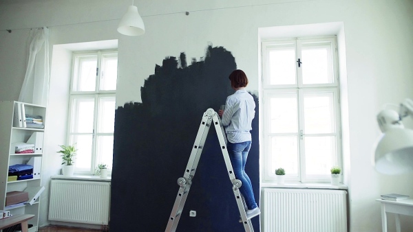 A young woman painting wall black. A startup of small business. Slow motion.