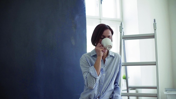 A young woman with coffee painting wall black. A startup of small business. Slow motion.