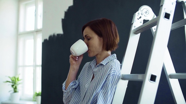 A young woman with coffee painting wall black. A startup of small business. Slow motion.