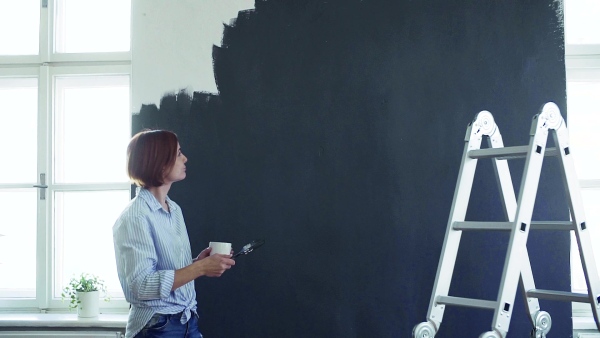 A young woman painting wall black. A startup of small business. Slow motion.