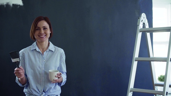 A young woman painting wall black. A startup of small business. Slow motion.