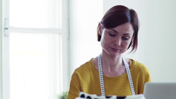 Young creative woman with laptop working in a studio, startup of small tailoring business.