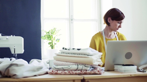 Young creative woman with laptop working in a studio, startup of small tailoring business. Slow motion.