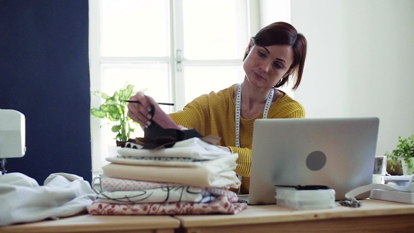 Young creative woman with laptop working in a studio, startup of small tailoring business. Slow motion.