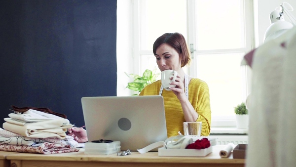 Young creative woman with laptop working in a studio, startup of small tailoring business. Slow motion.