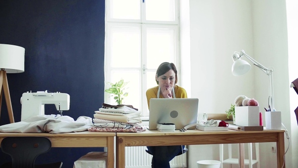 Young creative woman with laptop working in a studio, startup of small tailoring business. Slow motion.