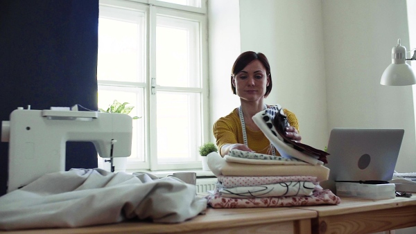 Young creative woman with laptop working in a studio, startup of small tailoring business. Slow motion.