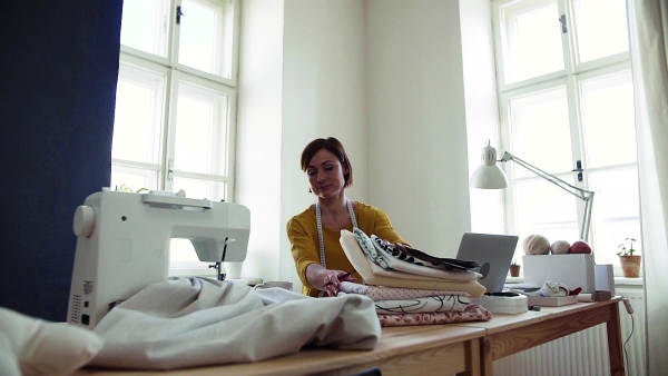 Young creative woman with laptop working in a studio, startup of small tailoring business. Slow motion.