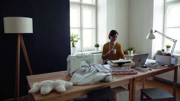 Young creative woman with laptop working in a studio, startup of small tailoring business. Slow motion.