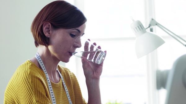 Young creative woman working in a studio, drinking water. A startup of small tailoring business.