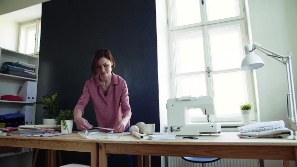 Young creative woman in a studio, working. A startup of small tailoring business. Slow motion.