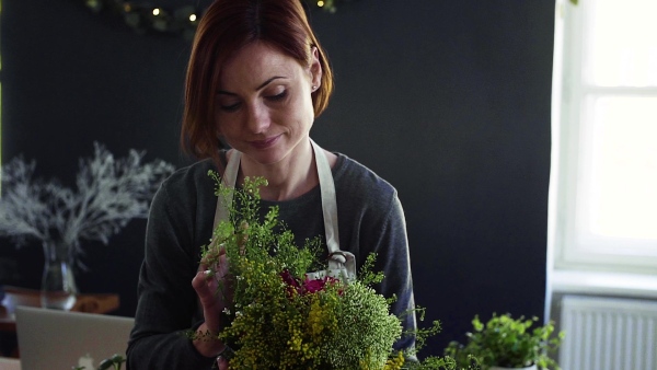 A young creative woman arranging flowers in a flower shop. A startup of florist business. Slow motion.