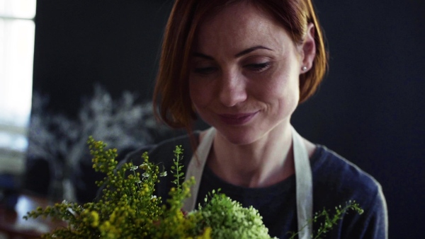 A close-up of young creative woman arranging flowers in a flower shop. A startup of florist business. Slow motion.